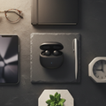 Premium wireless earbuds with smart charging case on dark slate surface with minimalist desk accessories